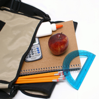 Aus einer liegenden, grauen Schultasche sind ein Block, ein paar gelbe Bleistifte, ein Apfel, ein Taschenrechner und ein Lineal herausgefallen.